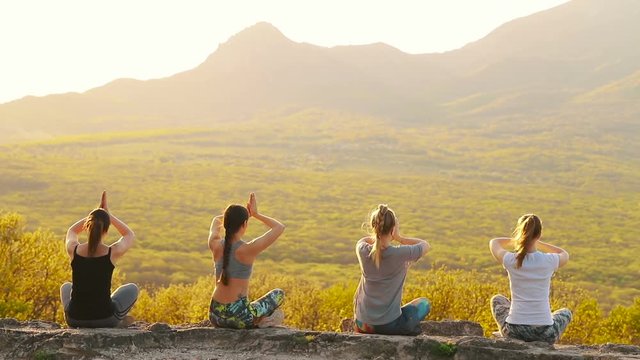 A group of girls at sunset are engaged in yoga. Slow motion