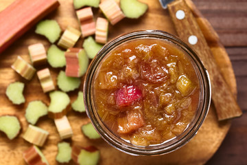 Homemade rhubarb jam in jar with raw cut rhubarb on the side, photographed overhead (Selective Focus, Focus on the jam)