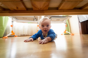 Funny portrait of amazed toddler boy lying on floor and looking under the bed