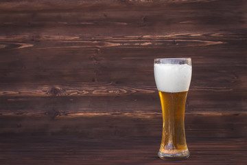 Glass of cold beer on a brown wooden background.