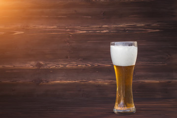 Glass of cold beer on a brown wooden background.