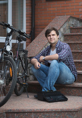 Fototapeta na wymiar Smiling young man sitting on house porch and repairing bicycle