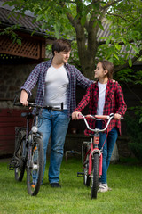 Young man with teenage girl standing with bicycles at house backyard