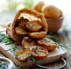 Baked potatoes. Baked halves of potatoes seasoned with rosemary and sea salt on a wooden rustic table. Vegetarian food