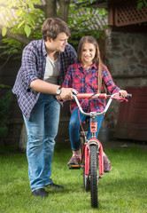 Fototapeta na wymiar Young handsome man teaching his daughter riding adult bicycle at park