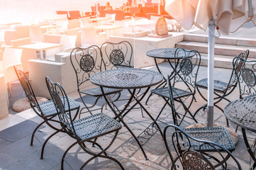 Openwork tables and chairs of outdoor cafes await visitors in the summer. Cozy old cafes on the street of the summer city