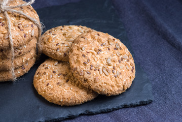 homemade oat cookies with sunflower seeds on shale board and dark blue textile background