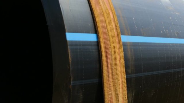 Large plastic sewer pipe with a blue stripe on the side of PEX wrapped in webbing, lying on the sand outside, on the street, on the site. Zoom in, dry season, summer, day, Sunny, natural light, close-