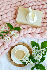 Cup with white coffee, milk, pink pastel giant blanket, bedroom, morning concept, bird cherry tree flowers, book reading 