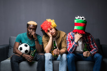 Three friends fanatic football fans watching soccer game on television with beer bottles and pizza suffering stress and crazy nervous on couch sad and dejected as if their team is loosing