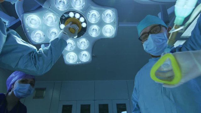 Low Angle Shot Falling Asleep POV Patient View: Two Professional Surgeons Turning on Surgery Lights while Anesthesiologist Puts on Anesthesia Mask. Shot on RED EPIC-W 8K Helium Cinema Camera.