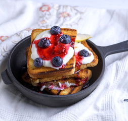 French toast with berries, syrup and sour cream in a black cast-iron frying pan