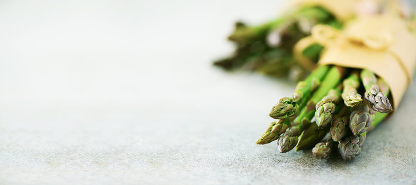 Fresh green asparagus in craft paper on marble background. Banner. Raw, vegan, vegetarian and clean eating concept. Food frame with copy space