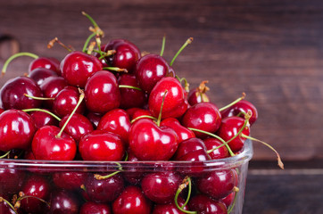 Fototapeta na wymiar Sweet red cherries in glass bowl on dark wooden backgound with copy space. Summer and harvest concept. Vegan, vegetarian, raw food