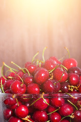 Sweet red cherries in glass bowl on dark wooden backgound with copy space. Sunny summer and harvest concept. Sunlight effect. Vegan, vegetarian, raw food