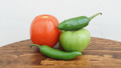 Chiles, chiles serranos, chiles habaneros, tomates y jitomtes frescos sobre mesa de madera con fondo blanco