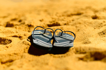 Summer slippers. Navy blue flip flop on yellow sand beach background. Copy space, top view. Holiday...
