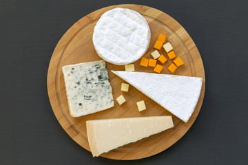 Wooden board with various types of cheese, top view. Dark background. Flat lay. From above.