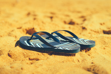 Summer slippers. Navy blue flip flop on yellow sand beach background. Copy space, top view. Holiday...