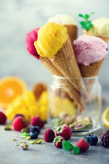 Colorful red, pink, yellow, green, white ice cream balls in waffle cones with different flavors - mango, lime, mint, pistachio, orange, strawberries, raspberries, blueberries. Summer concept