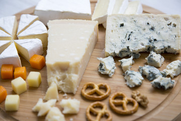 Delicious cheeses: camembert, blue cheese, brie, parmesan, mimolette and edam with pretzels and walnuts on round wooden board. Food for wine. Closeup.
