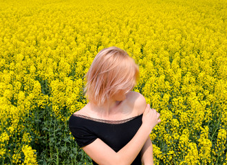 Fototapeta premium A girl in a black dress in a field of flowering rape.