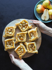 Puff pastry pies with pear on a black table. Homemade pastries on a round cutting board . The view from the top.