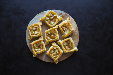Puff pastry pies with pear on a black table. Homemade pastries on a round cutting board . The view from the top.