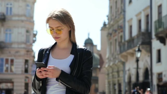 calm thoughtful woman using smart phone telephone on sunny street old buildings on blur background digital device internet addiction online communication checking news message stylish casual look