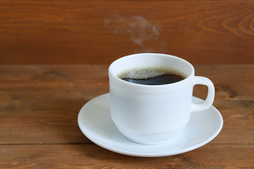Hot coffee in a white cup on a saucer against a wooden background. Close-up.