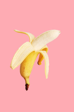 Half peeled banana on a pink background.