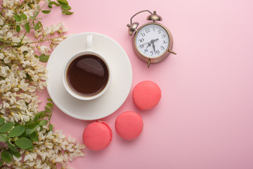 Spring floral background with coffee and macaroons, and alarm clock. Flat white flowers on a light pink background, top view, copy space.