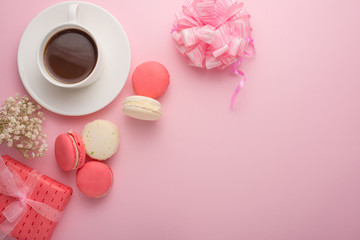 Flat-lay coffee with macaroons with a gift and flowers with an empty space for an inscription or a postcard on a holiday, on a light pink background