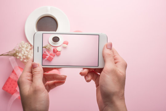 Girl takes pictures on a phone on a pink background of coffee and macaroons, for an instagram