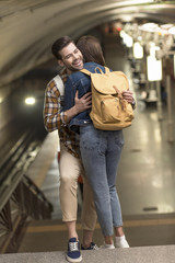 Naklejka premium stylish male tourist with backpack hugging girlfriend at subway station