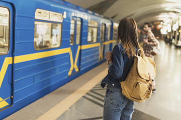 rear view of stylish female tourist with backpack standing at subway station