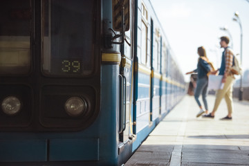 closeup shot of train and couple of tourists behind at outdoor subway station