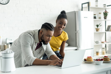 african american couple using laptop at kitchen