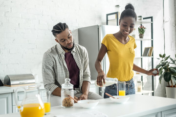 african american girlfriend pouring milk into plate at kitchen