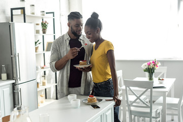 african american boyfriend feeding girlfriend with strawberry at kitchen