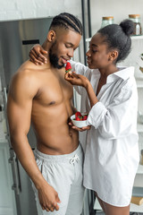 african american girlfriend feeding boyfriend with strawberry at kitchen