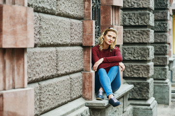 Fototapeta na wymiar A young woman on a city street . Stylish lady in jeans and Burgundy sweater in the city . The concept of casual wear