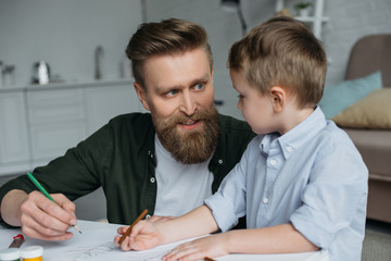 father and cute little son with colorful pencils drawing pictures together at home