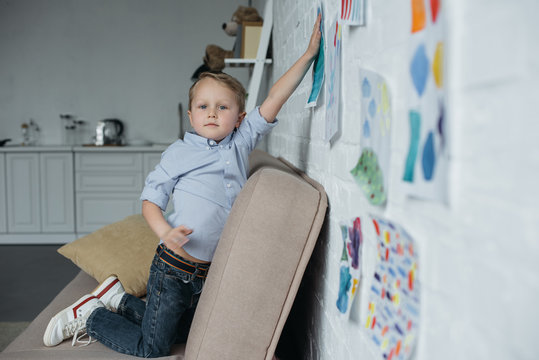 side view of little kid hanging childish pictures on wall at home