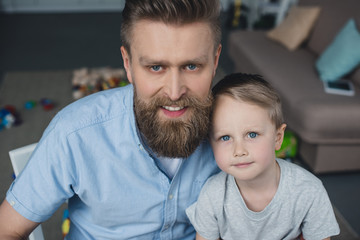 portrait of smiling father and son looking at camera at home
