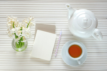 Morning tea flat lay.tea with blank notebook, daffodil flower on a light wooden  background.  top view, copy space