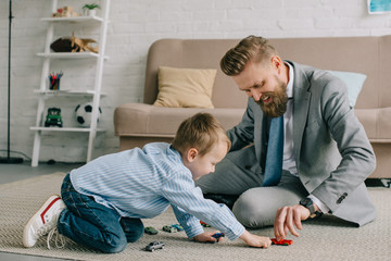businessman in suit and little son playing with toy cars on floor at home, work and life balance...