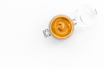 Nut butter, peanut butter in glass jar on white background top view copy space