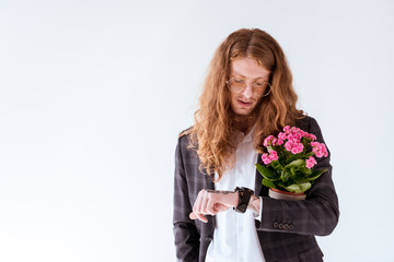 stylish tattooed businessman with curly hair holding potted flowers and checking time isolated on white