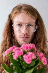 portrait of stylish man with curly hair with bouquet of pink flowers looking at camera